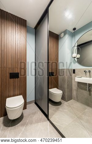 Modern Bright Bathroom With White Toilet Seat On Wooden Lamela Wall. Mirror On Grey Wall.