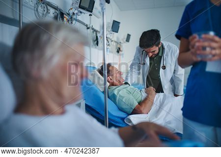 Young Nurse Giving Glass Of Water To Senior Patient, Doctor Laughing With Patient At Hospital Ward.