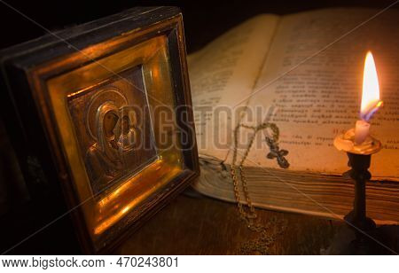 A Candle Illuminates The Icon Of The Virgin Mary And A Cross On A Chain Lying On An Open Psalter