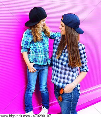 Fashion Mother Looking At Child Little Girl In Checkered Shirts And Baseball Caps In City On Colorfu