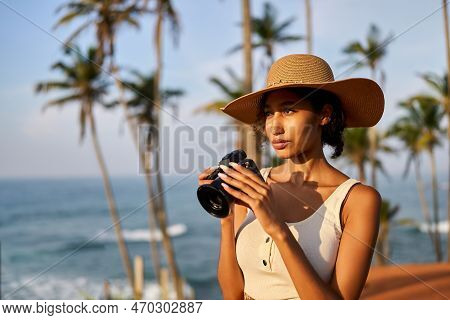 Young African Female Model Tourist With Camera In Colorful Clothes And Straw Hat Taking Pictures At 