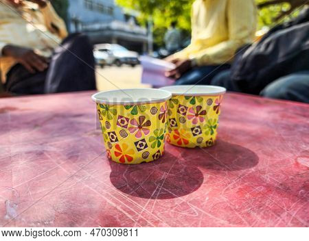 Stock Photo Of Empty Yellow Color Floral Design Printed Two Paper Cup Kept On Red Color Plastic Tabl