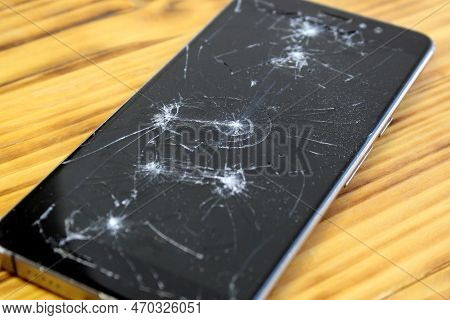 A Broken Black Cell Phone Lies On A Wooden Table.