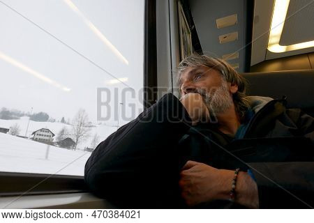 Pensive Mature Passenger Looking Out The Train Window , Snowy Landscape Outside