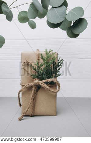A Gift Wrapped In Brown Paper And Decorated With A Thuya Branch On A Gray White Wooden Background Wi
