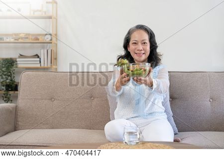Happy Old Woman Eating Healthy Vegetable Salad At Home