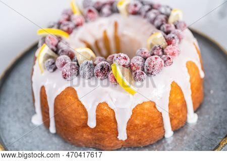Lemon Cranberry Bundt Cake Decorated With Sugar Cranberries And Lemon Wedges On A Cake Stand.