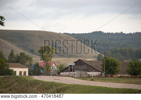 An Old Barn Sits In The Middle Of A Rural Area, Hill And Forest On Background