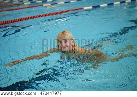 Happy Woman 60-65 Years Old Swims At A Sports Public Pool. The Concept Of Slow Aging And The Fullnes