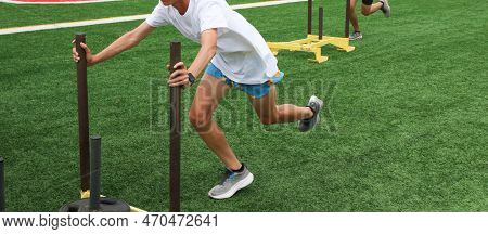 Two Runners Pushing Sleds With Weights On A Turf Field During Summer Pre Season Practice.