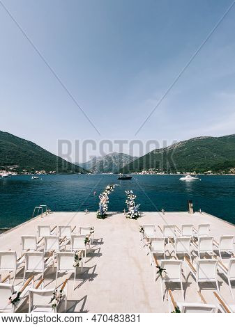 Rows Of Chairs Decorated With Flowers Stand On The Pier Near The Wedding Semi-arch