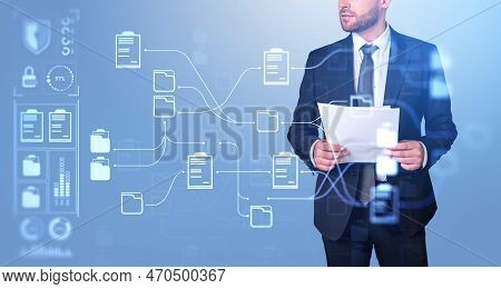 Serious Businessman In Formal Suit Standing Holding Documents And Watching At Digital Interface With