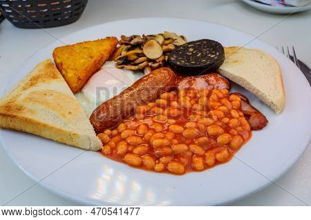 White Board With Full English Breakfast With Bacon, Fried Egg, Beans, Tomato, Roasted Sausage, Black