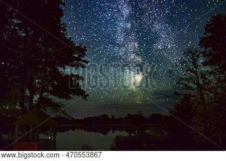 The Starry Sky Over The Forest Lake. The Milky Way Stretches Across The Sky, The Stars Are Reflected