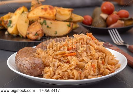 Braised Cabbage - Bigos And Grilled Sausage In A White Porcelain Plate Against The Background Of Rus
