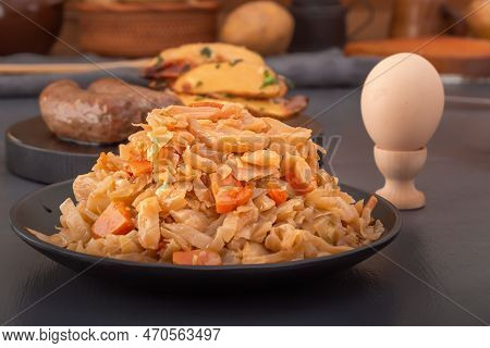 Stewed Cabbage - Bigos In A Black Plate On The Background Of A Boiled Chicken Egg And Baked Potatoes