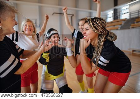 Group Of Young And Old Cheerful Women, Floorball Team Players, In Gym Cebrating Victory.