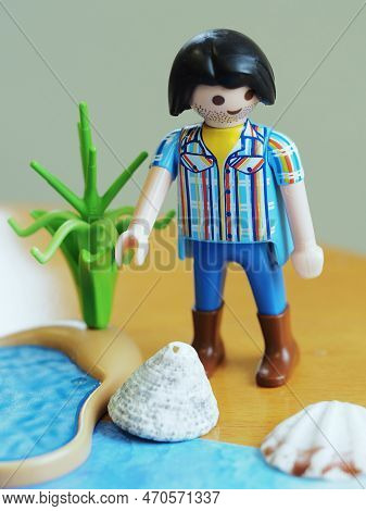 A Toy Doll On The Shore Of A Beach, Playing With A Shell From The Sea.