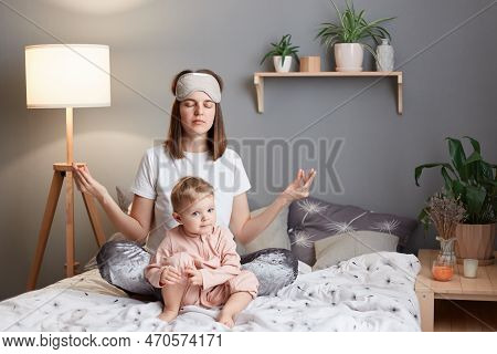 Image Of Exhausted Mother And Infant Kid At Home, Woman Sitting In Lotus Pose And Practicing Yoga, T