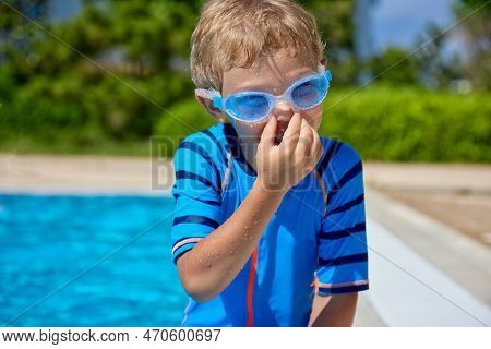 Funny Boy In Swimming Glasses Is Sitting By The Pool, Laughing, Pinching His Nose With His Fingers, 