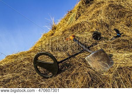 Metal Detector And Sapper Shovel On A Haystack In An Open Field Against The Blue Sky