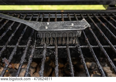 Cleaning A Dirty Grill While Standing On The Terrace And Emptying The Ashes.