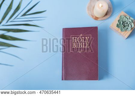 Christian Holy Bible And Palm Leaf With сandle On Blue Background, Flat Lay, Top View.