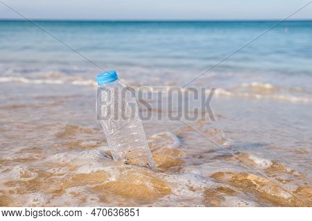 Empty Plastic Bottle From Drinking Water In Sea Waves And Sand. The Problem Of Ocean Plastic Polluti