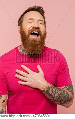 Cheerful Bearded Man Touching Chest And Laughing With Closed Eyes Isolated On Pink.