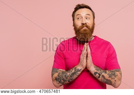 Smiling And Tricky Man In Magenta T-shirt Showing Please Gesture And Looking Away Isolated On Pink.