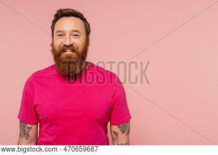 Positive Bearded And Tattooed Man In Magenta T-shirt Smiling At Camera Isolated On Pink.