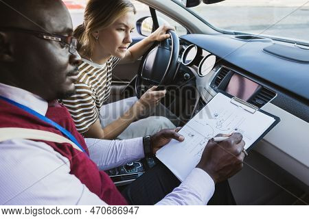 Driving School Concept. A Car Instructor Teaches A Young Woman How To Drive. Teaching The Rules Of T