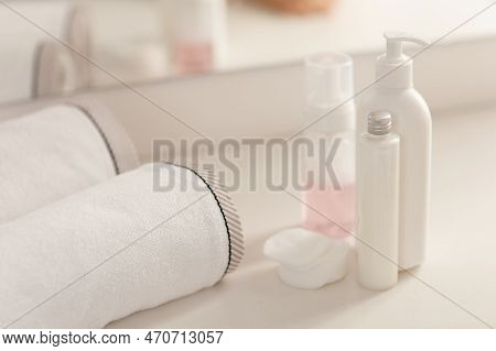 Set White Plastic Cosmetic Bottles With Cream Soap And Towel On White Table At Bathroom.