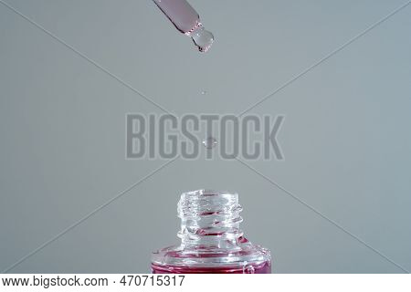 Pink Face Oil Drop From Glass Pipette Dropper. Macro Close Up For Cosmetic Neutral Background Bakuch