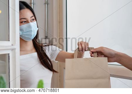 Smiling Young Asian Woman,client Accepting A Delivery Of Bag, Cardboard Box From Delivery Man Wearin
