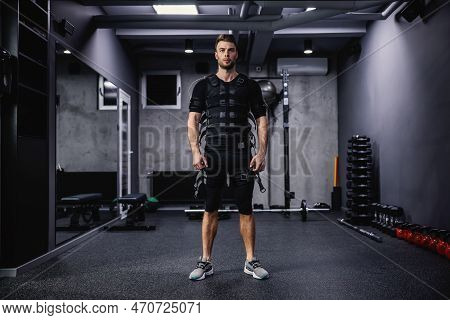 A Confident Male Instructor Dressed In A Special Suit For Ems Technology Stands In The Gym With A Da