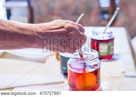 Old Woman Dyeing Easter Eggs At Home In The Kitchen In The Cucumber Glass And With Different Colors,