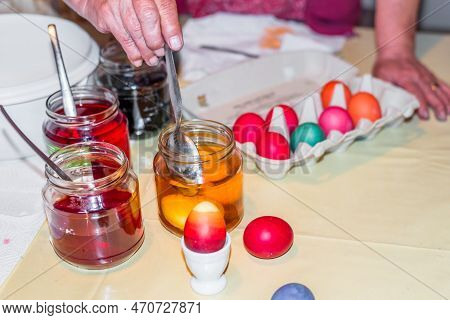 Old Woman Dyeing Easter Eggs At Home In The Kitchen In The Cucumber Glass And With Different Colors,
