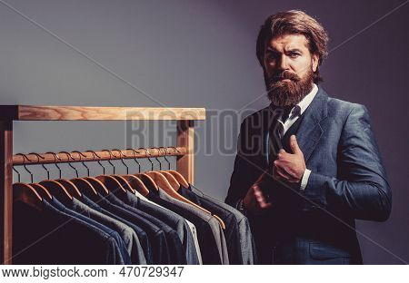 Male Suits Hanging In A Row. Men Clothing, Boutiques. Handsome Bearded Fashion Man In Classical Cost
