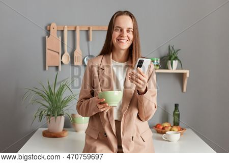 Portrait Of Charming Cute Happy Young Adult Woman Wearing Beige Suit Standing Near Table On Kitchen 