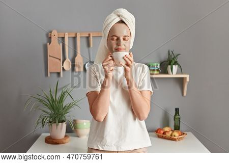 Indoor Shot Of Calm Relaxed Young Adult Woman Wrapped White Towel And Dressed In T-shirt Standing Ne