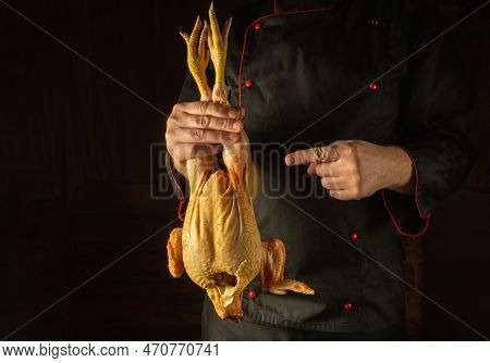 Raw Fresh Rooster In The Hand Of A Cook In A Restaurant Kitchen. Presentation Of A Cock Before Cooki