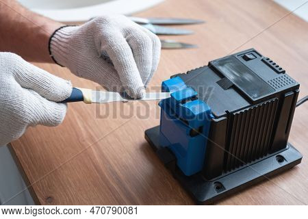 Sharpening A Knife On An Electric Sharpener At Home. The Man\'s Hand Drives The Knife Blade Between 