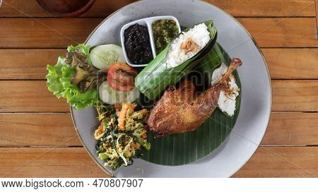 Crispy Black Fried Duck With Rice Covered In Banana Leaf, Some Veggetable And Special Mash Chili.