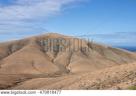 Shapes And Lines Of The Mountains Of The Volcanic Origin. Light Brown Color Of The Soil. Sky With Cl
