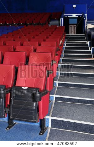 Rows of red and blue seats, entrance and stairs in auditorium in cinema theater.