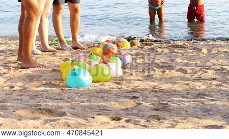 On The Beach, On The Sand Are Balloons Filled With Water Instead Of Air. People Having A Rest Playin