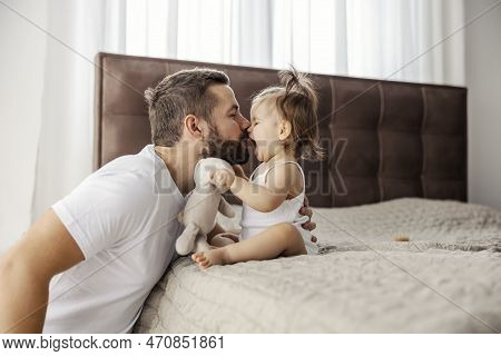 A Father Is Having Eskimo Kisses With His Daughter While She Is Sitting On A Bed.
