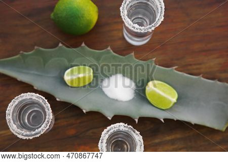 Mexican Tequila Shots, Salt, Lime And Green Leaf On Wooden Table, Flat Lay. Drink Made Of Agava