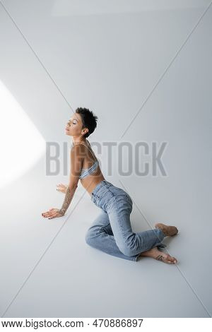 Barefoot Brunette Woman In Blue Jeans And Bralette Posing On Grey Background.